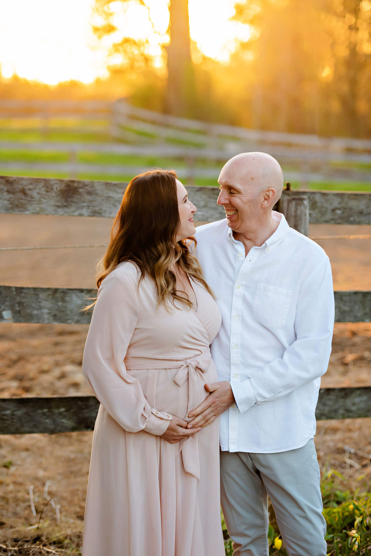 husband and wife looking at each other in front of a wood fence for their maternity session in Toronto, Ontario.