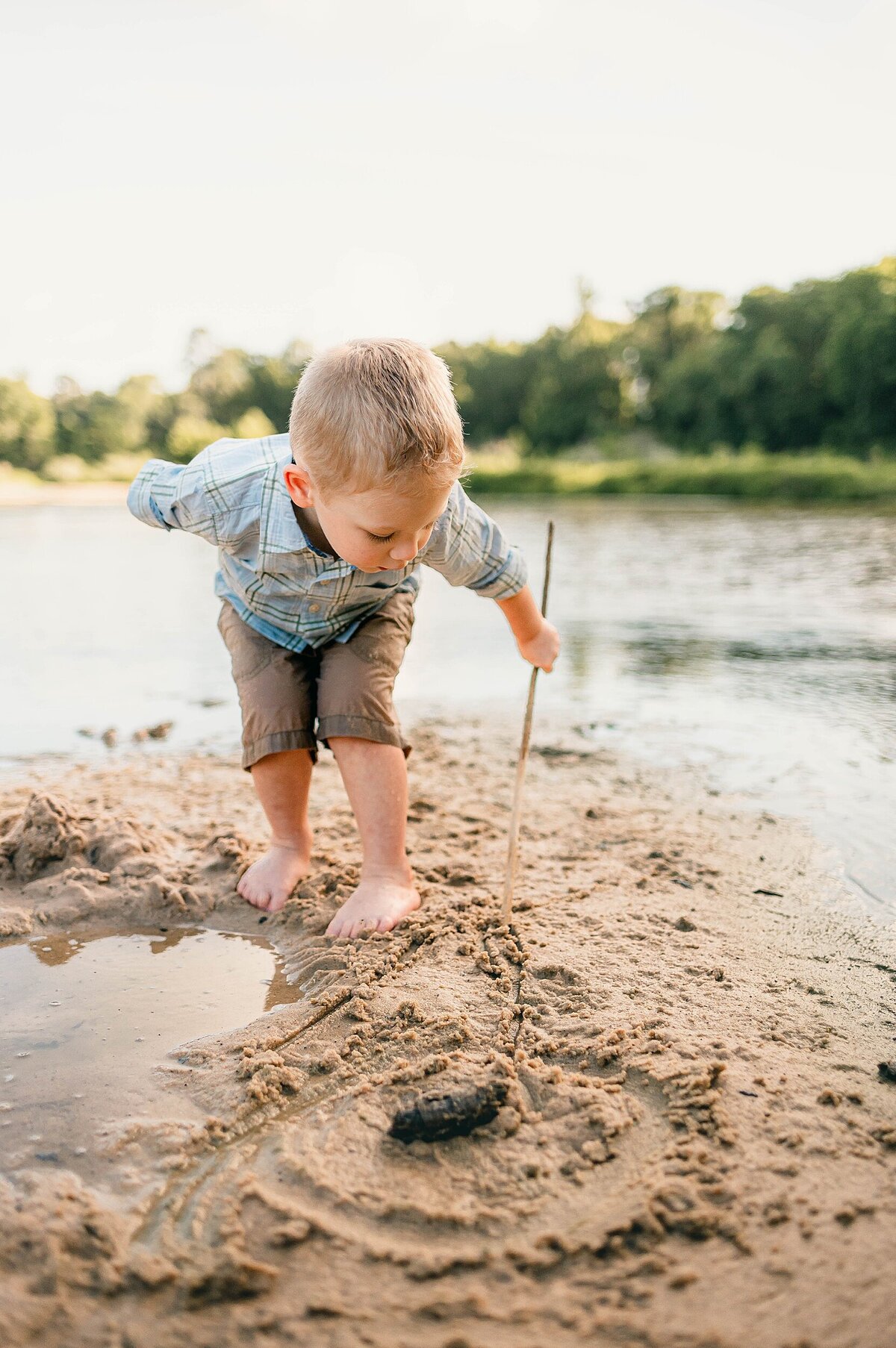 toddler boy with stick drawing circles in the sand by Cypress Family Photographer