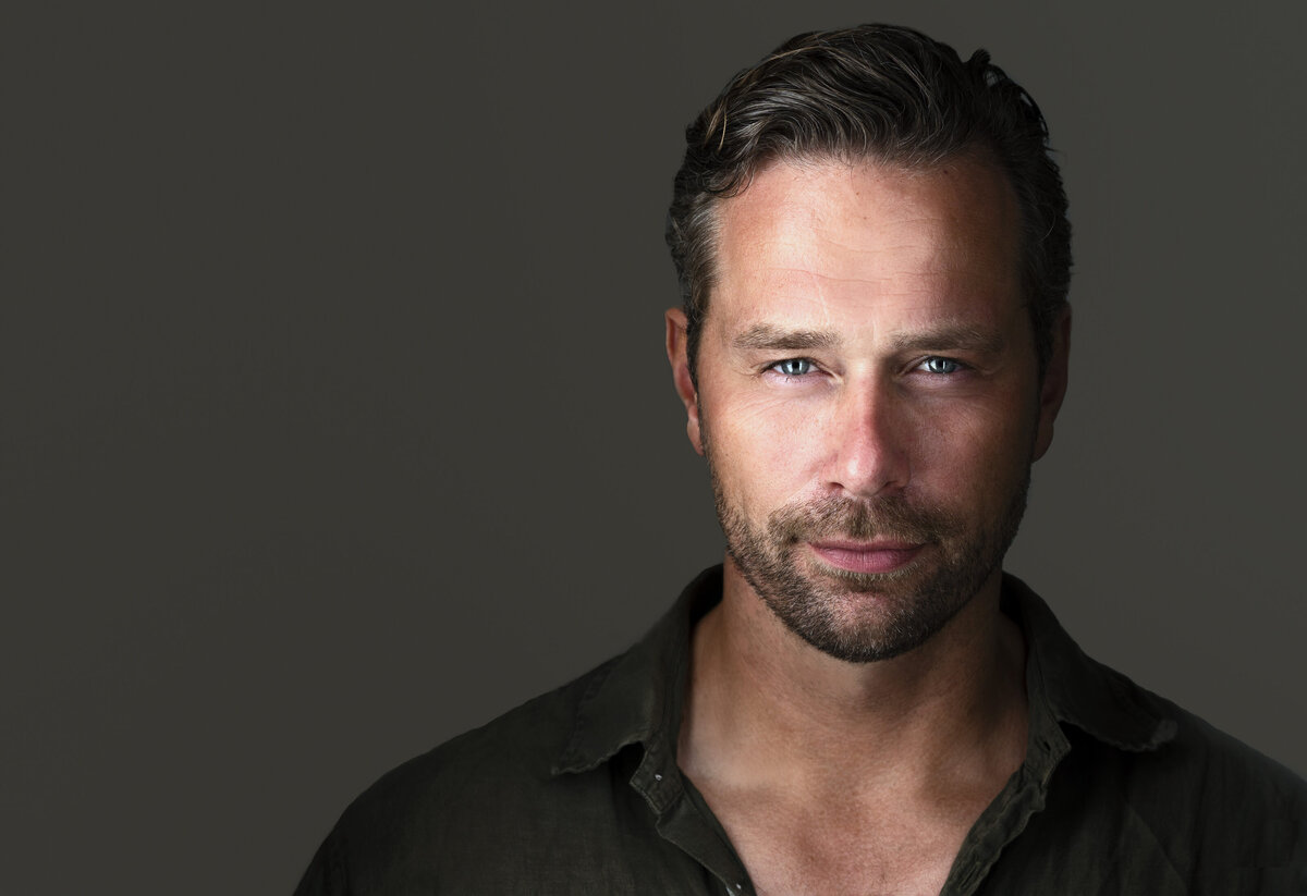 Headshot captured in Philadelphia, PA branding headshot studio. Man in black button down shirt is facing the camera with a closed-mouth smile and steely glare.