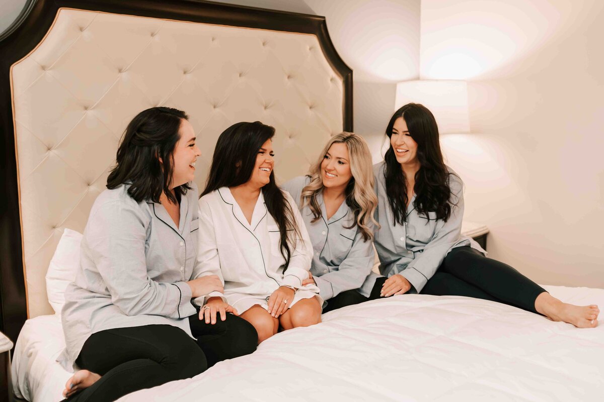 bride and her bridesmaids sit on bed at hotel, minutes before their wedding ceremony