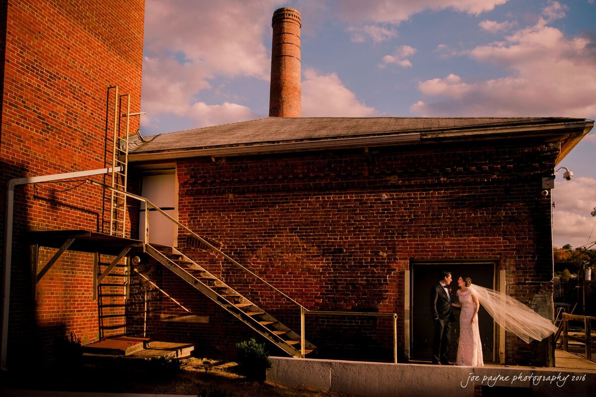 A bride and groom standing outside an industrial building together.