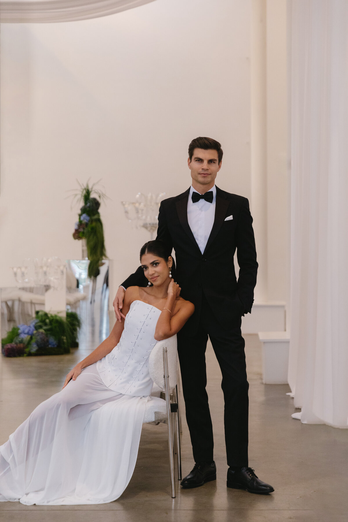 Bride seated with groom standing behind her, captured in a clean, minimalist ceremony setting with soft natural light.