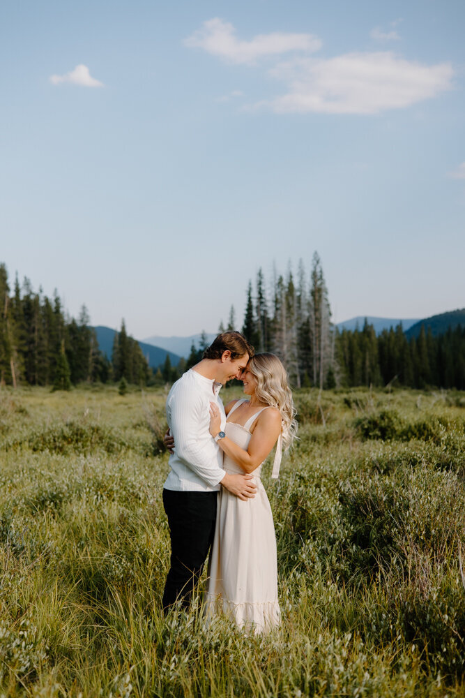 An engaged couple gently rests their foreheads together in a tender moment during their engagement session at Guanella Pass, Colorado. The natural beauty of the mountain landscape surrounds them, capturing the intimate and loving connection between the couple.