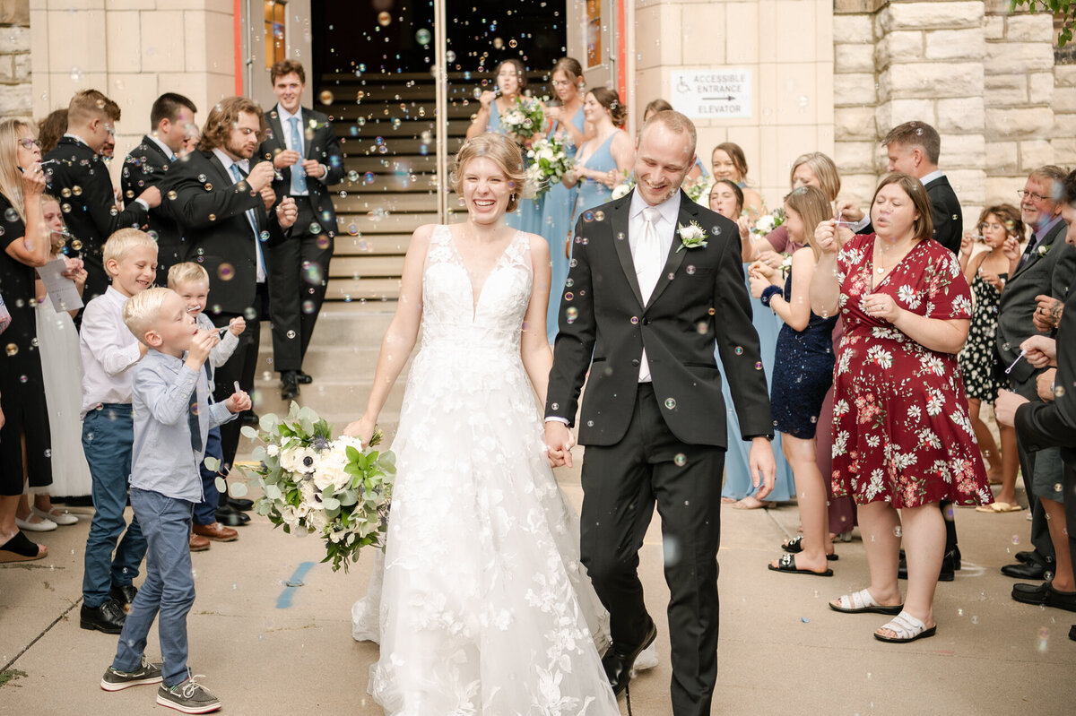 bride and groom hold hands while walking out of church and guests blow bubbles