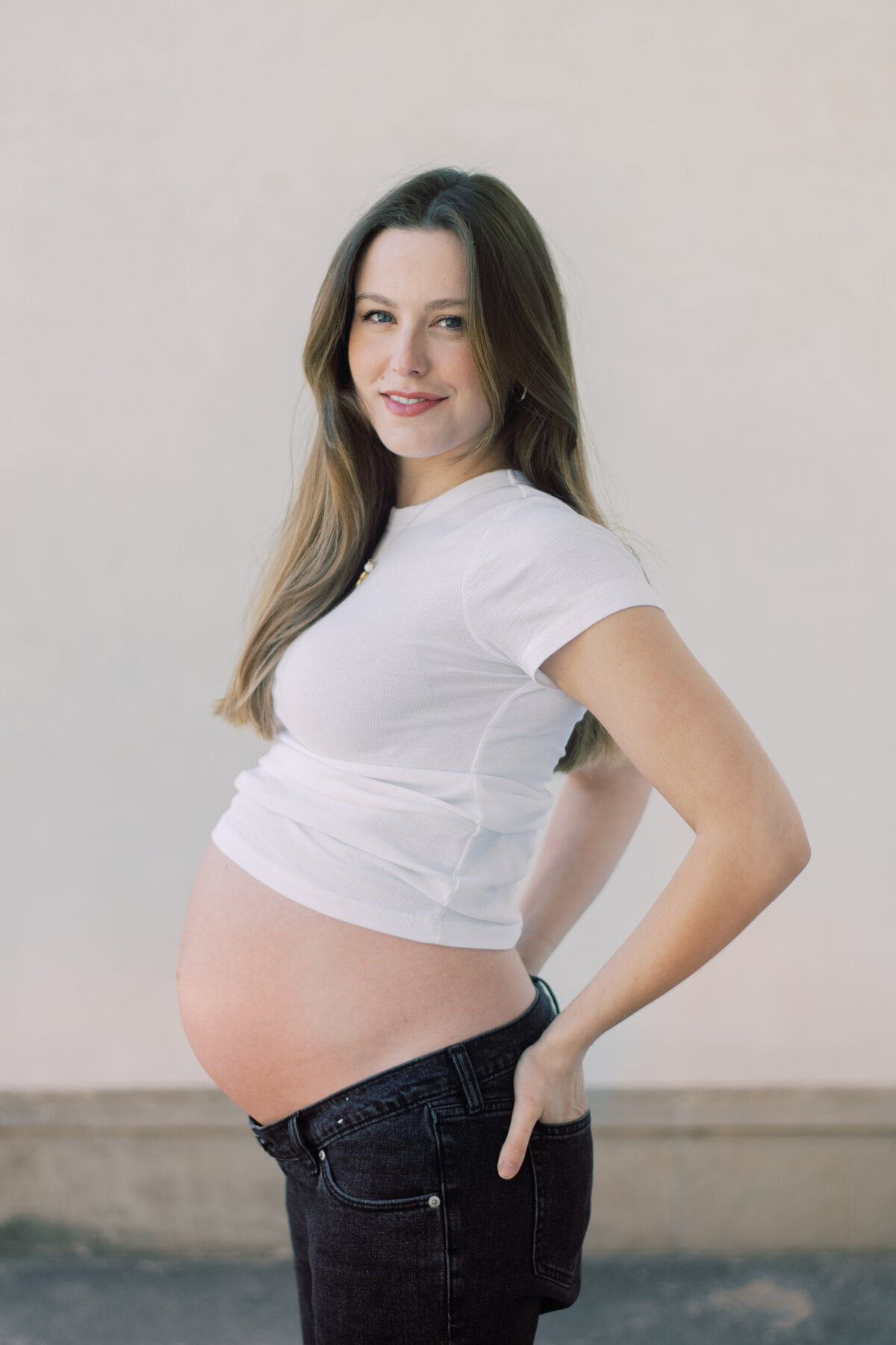Softly lit color image of a pregnant woman embracing her belly, styled in all-white Zara pieces
