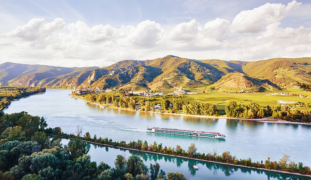 Panoramafotografie der Wachau mit vorbeifahrendem Donauschiff bei warmem Sonnenlicht – fotografiert vom Spezialisten für Alpenlandschaften, Atelier Schulte. Professionelle Landschaftsfotografie entlang der Donau in Niederösterreich mit Fokus auf Lichtstimmungen und regionale Atmosphäre.