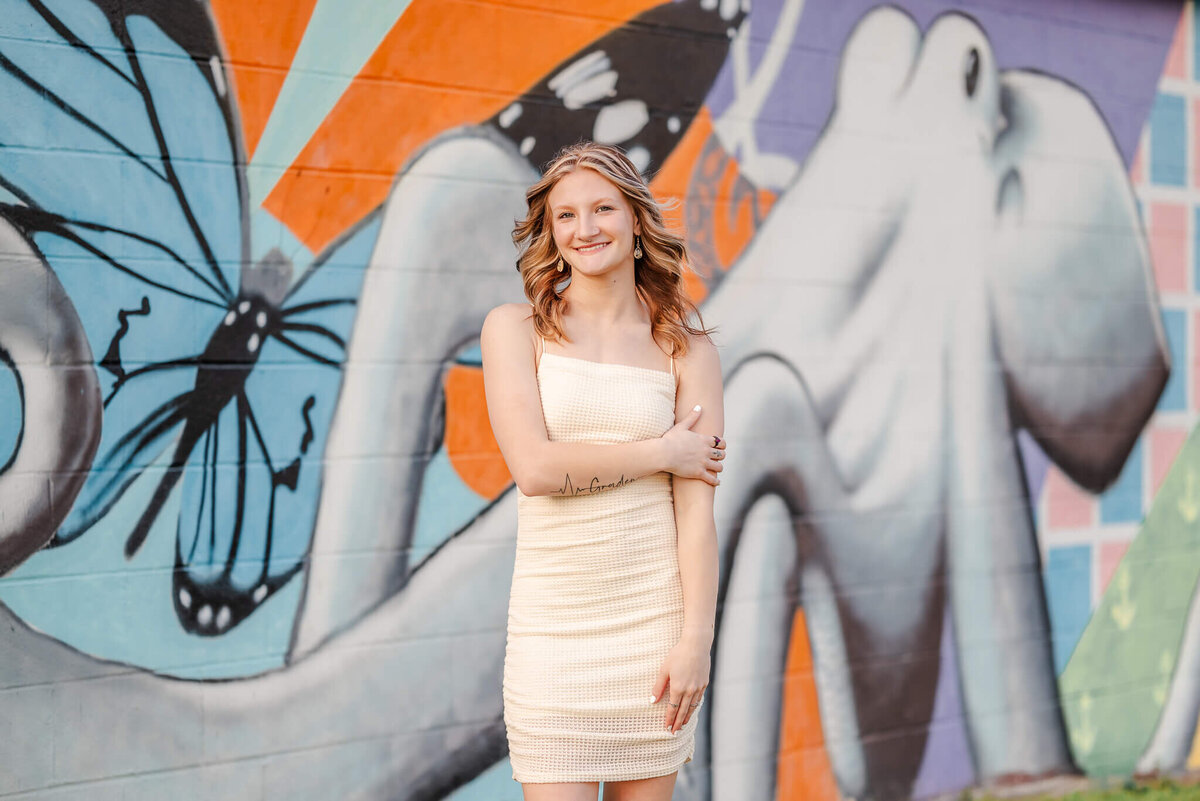 A high school senior, wearing and off-white bodycon dress, poses in front of a mural featuring a squid.
