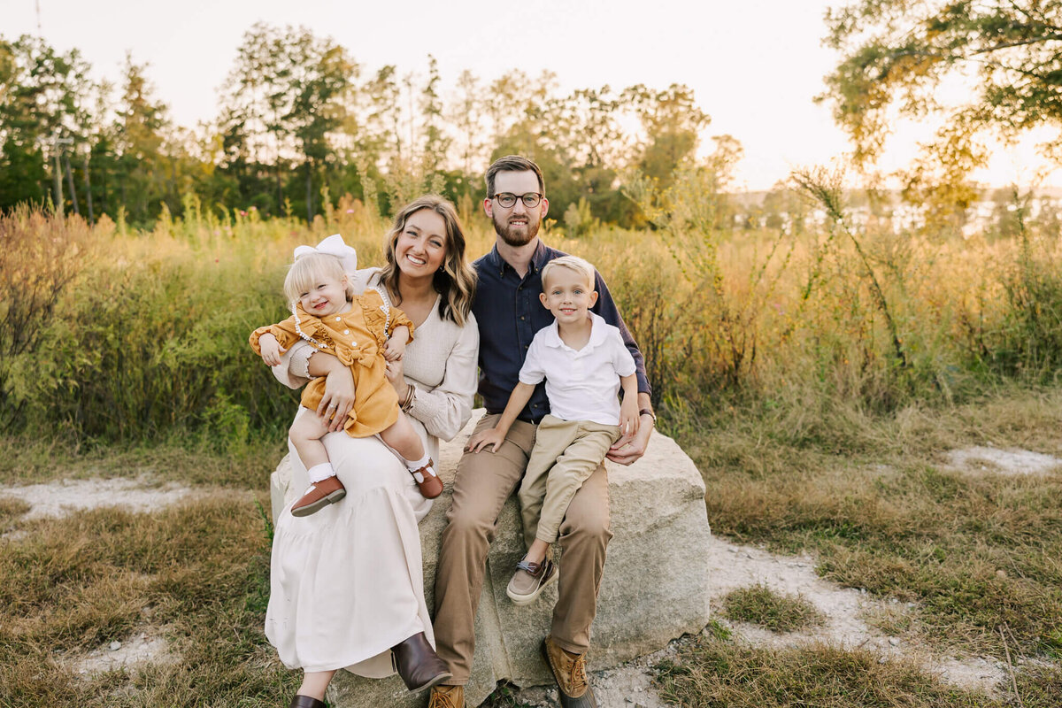Family of four sitting on a rock in an open field in Aiken, sc during their family session
