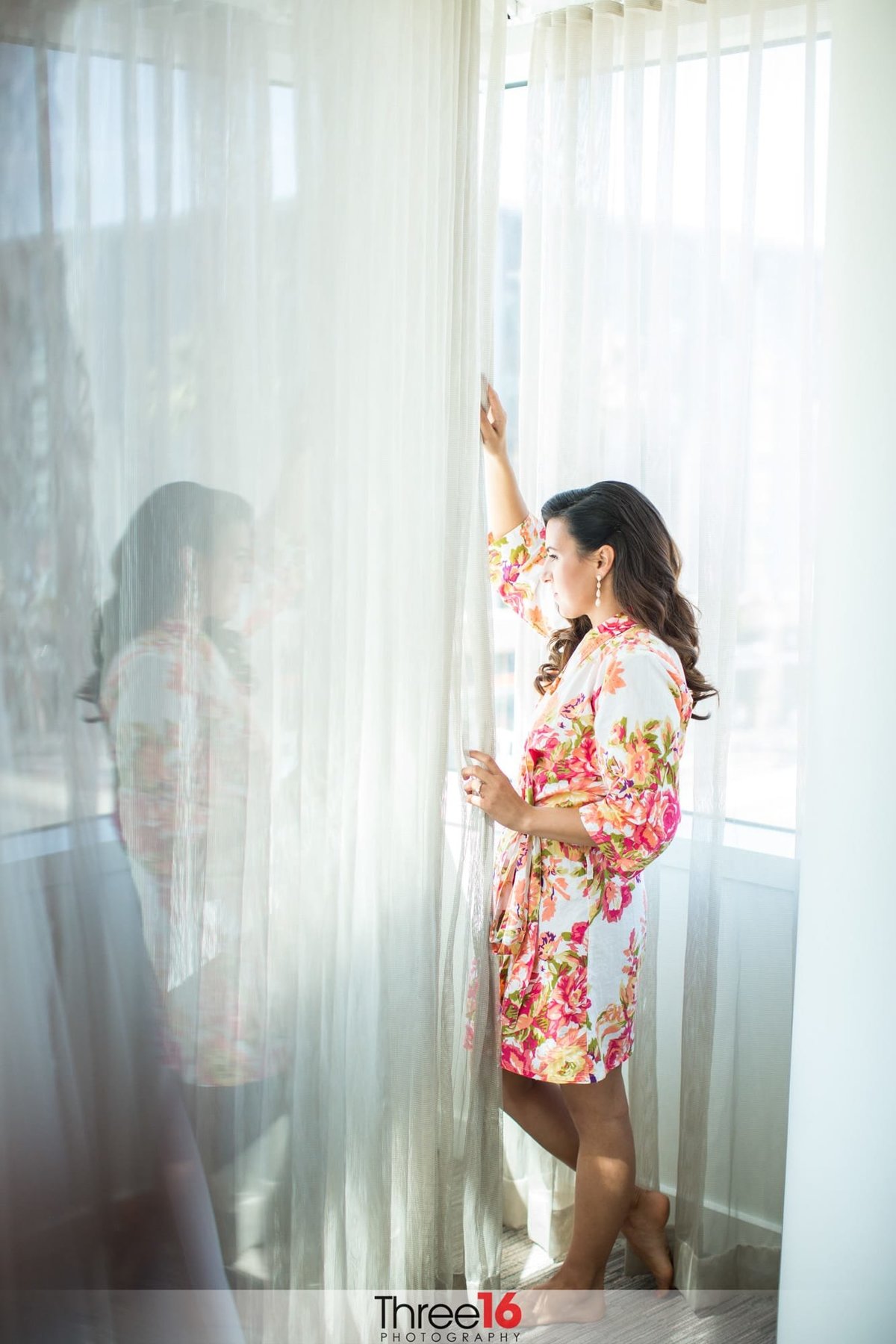 Bride looks out the window while still wearing her robe prior to the ceremony