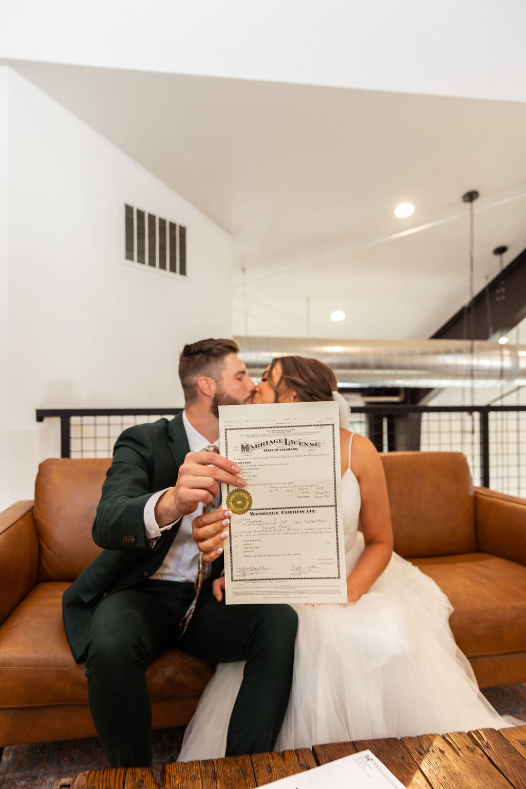 Bride and groom kiss with their marriage license on their wedding day.