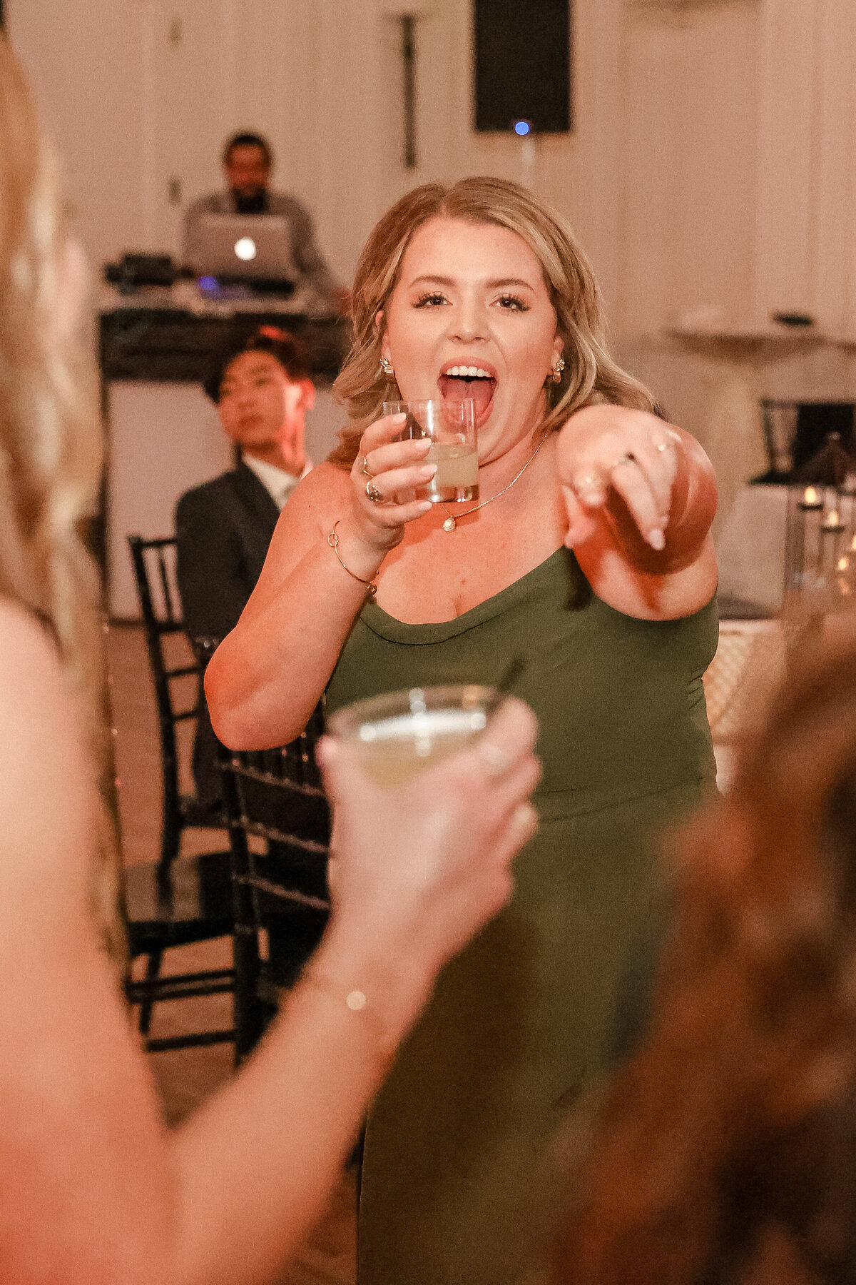 wedding guest with drink and blonde hair cheers  and points at wedding photographer
