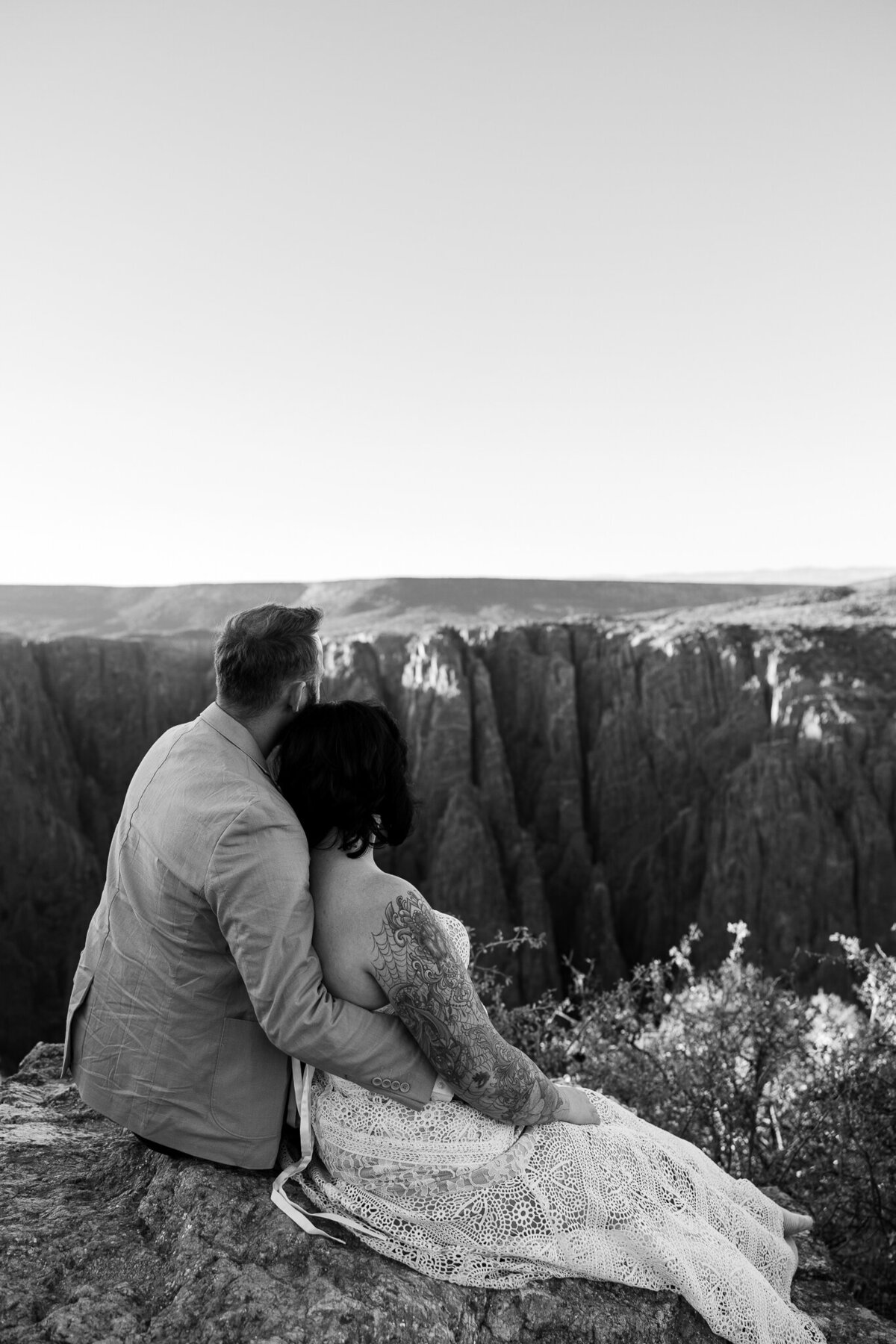 Black and white image of a couple sitting on the edge of a mountain cliff at Black Canyon National Park in Montrose, CO, capturing adventure and romance