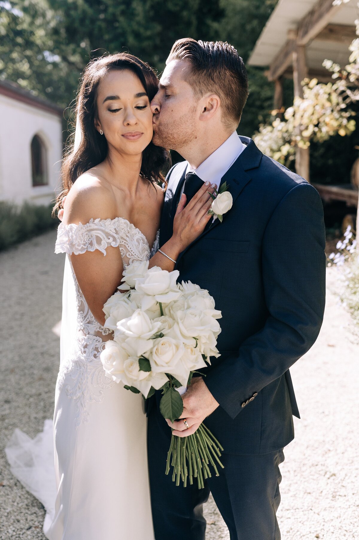 bride in lace off the shoulder dress with white roses bouquet from bourbon rose with husband in navy suit at trents vineyard