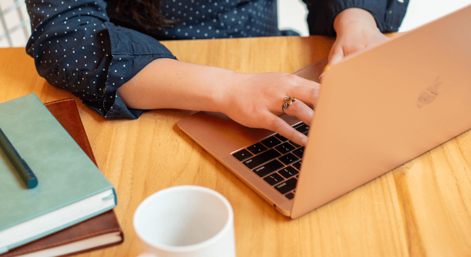 Hands typing on a laptop beside notebooks and a coffee mug, conveying focus and client work.