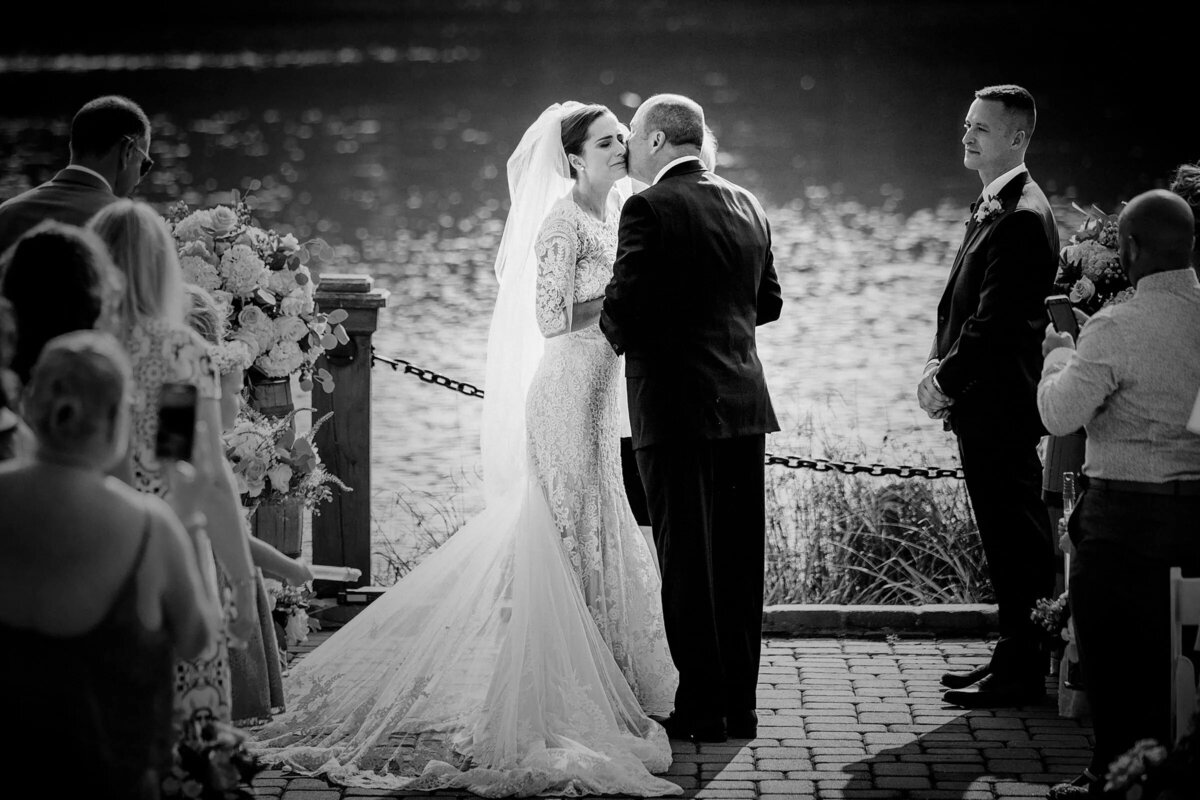 Bride and groom kissing at the altar by a lakeside with guests and a best man watching