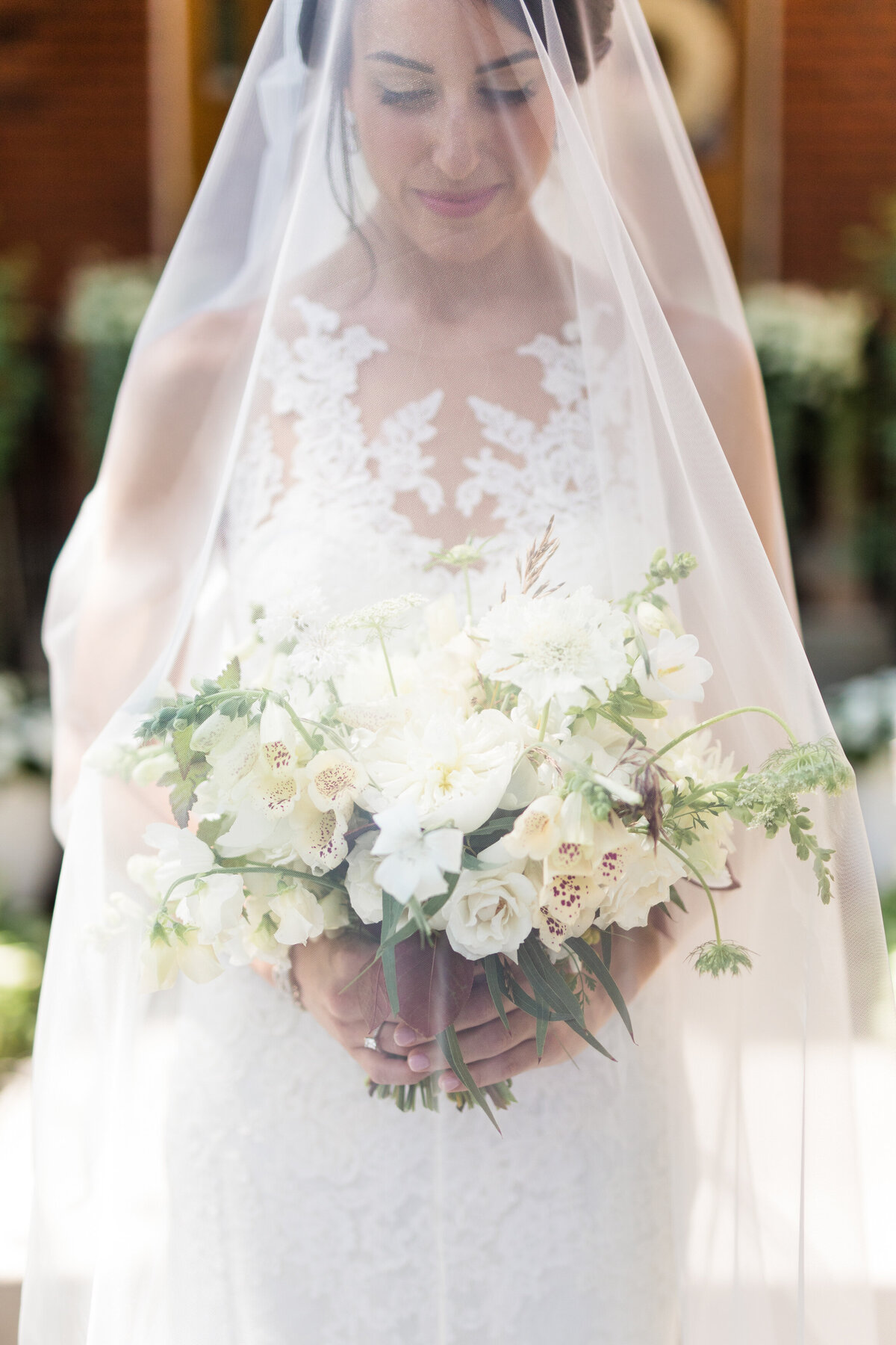 A bride holds an organic white flower bouquet under a long veil at a Montreal wedding.
