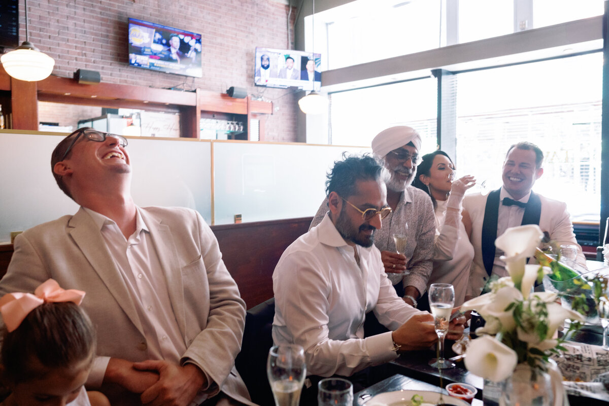 Candid photo of guests laughing and celebrating with champagne at Japna and Chris’s elopement reception.