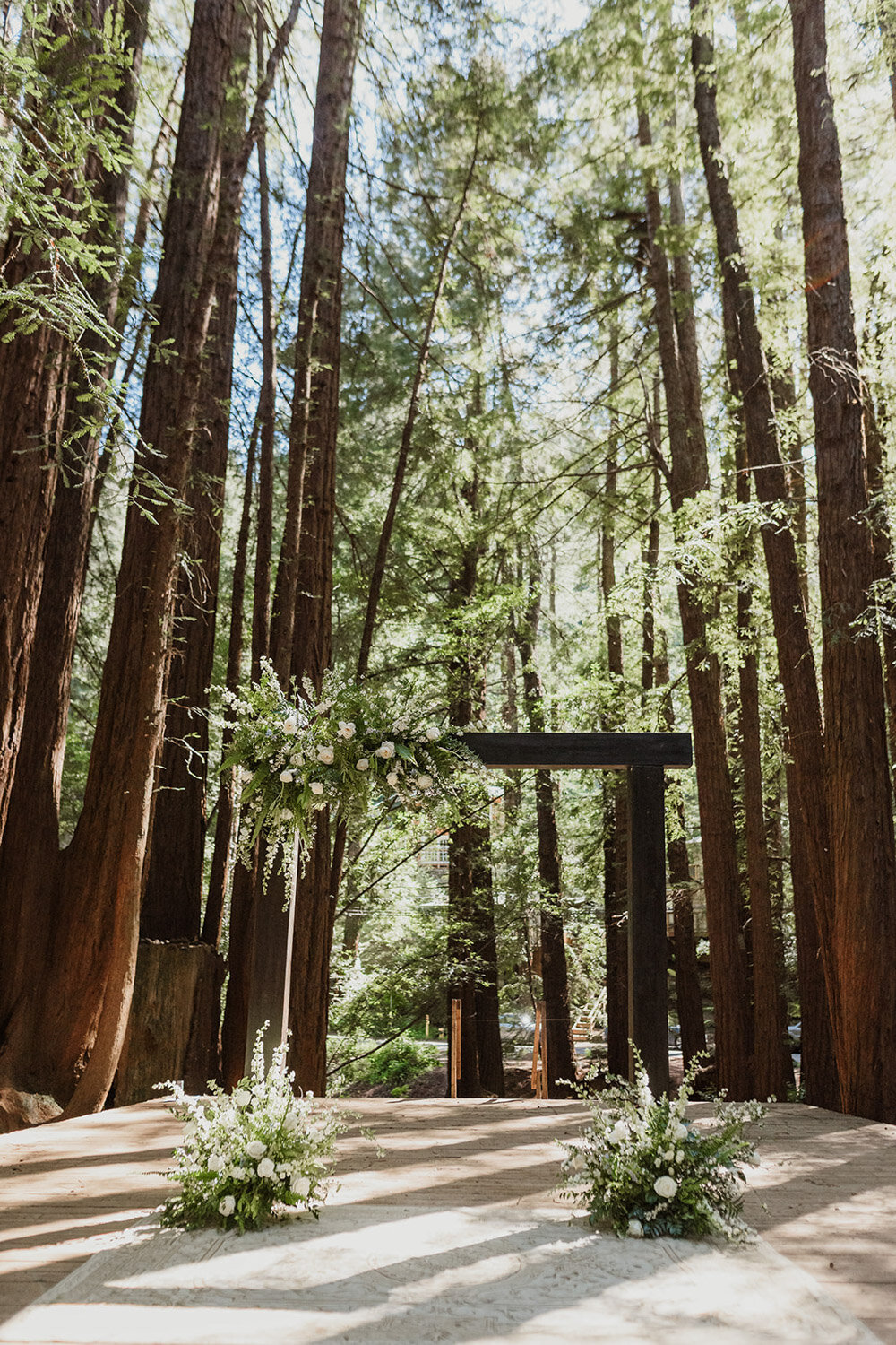Woodland wedding ceremony arch with greenery and white florals among tall redwoods