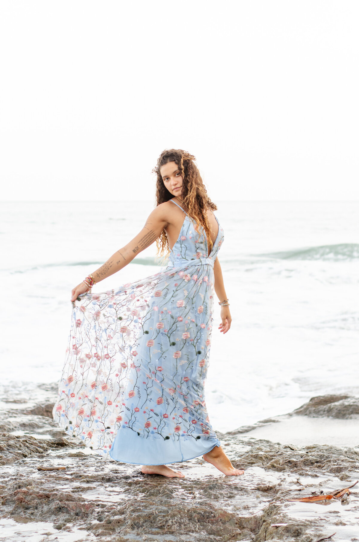 woman holds out her blue skirt on the beach