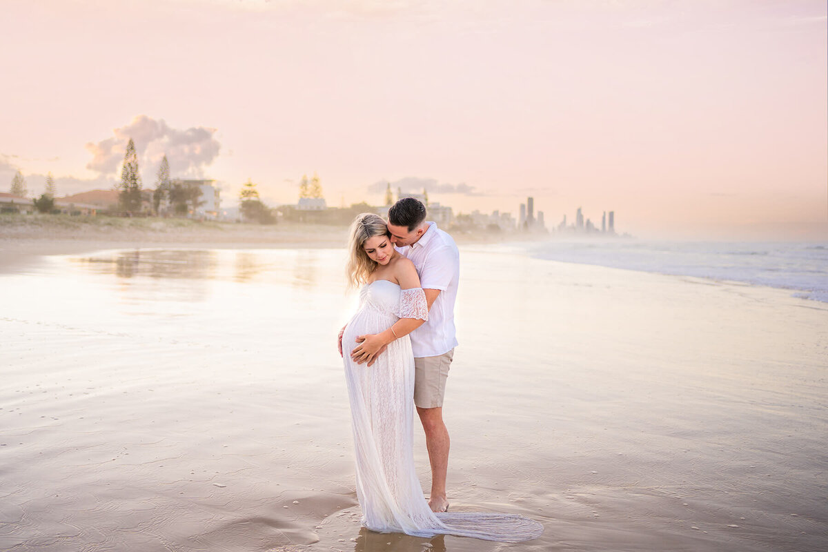 couple holding belly bump during maternity shoot in pink beach sunset Gold Coast