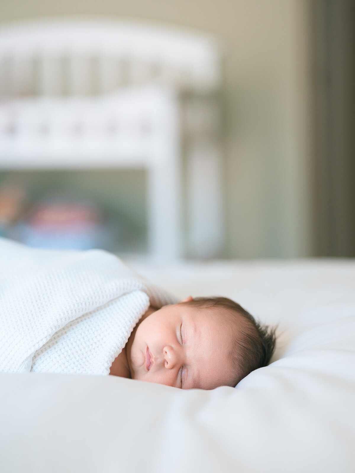 newborn baby swaddled with  white blanker sleeping peacefully on white bed in front of bedroom window captured by Menlo Park newborn photographer, Isela Lozano