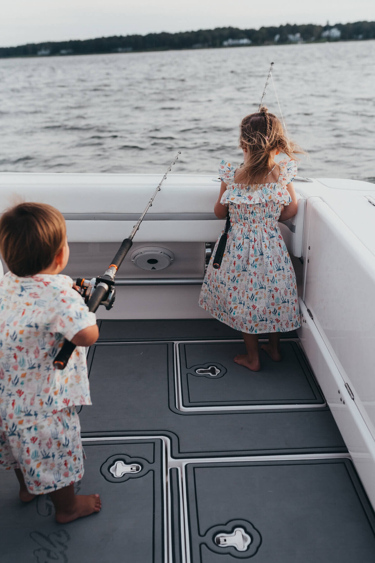 A brother and sister hold their father's deep sea fishing rods on their family boat at sunset