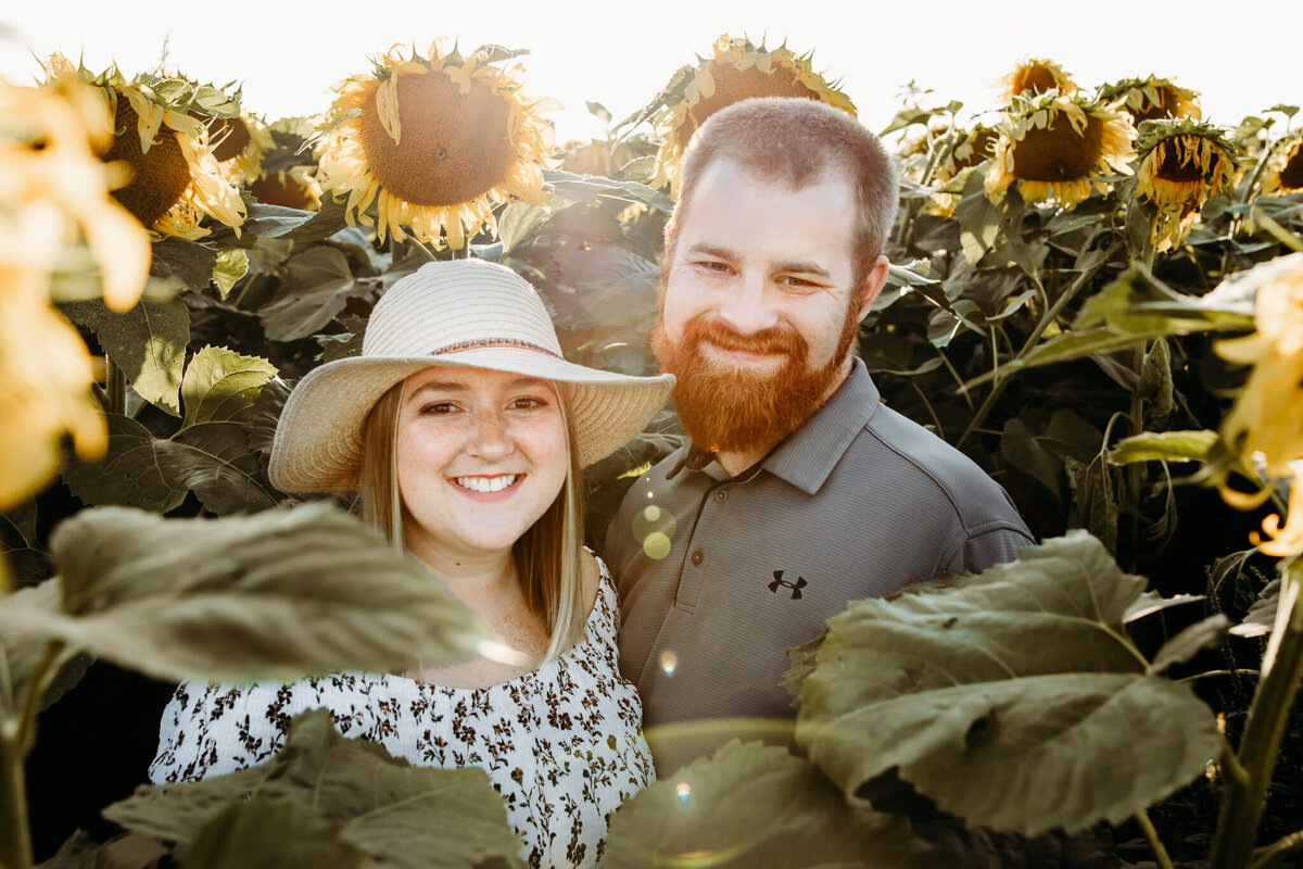 woman in sunhat and fiance smiling for photo in sunflower field