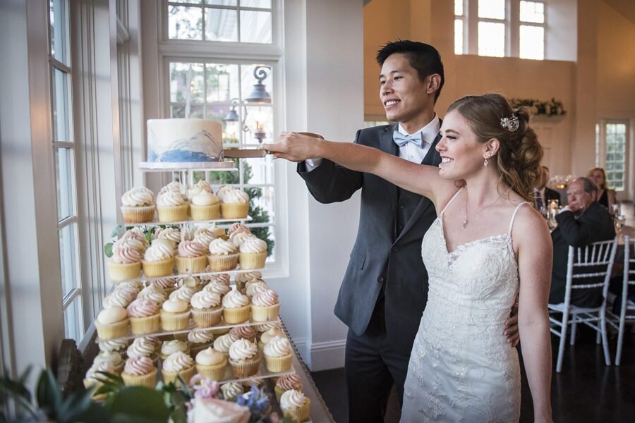A bride and groom cut their cake that is stacked on a 4-tier cupcake stand.