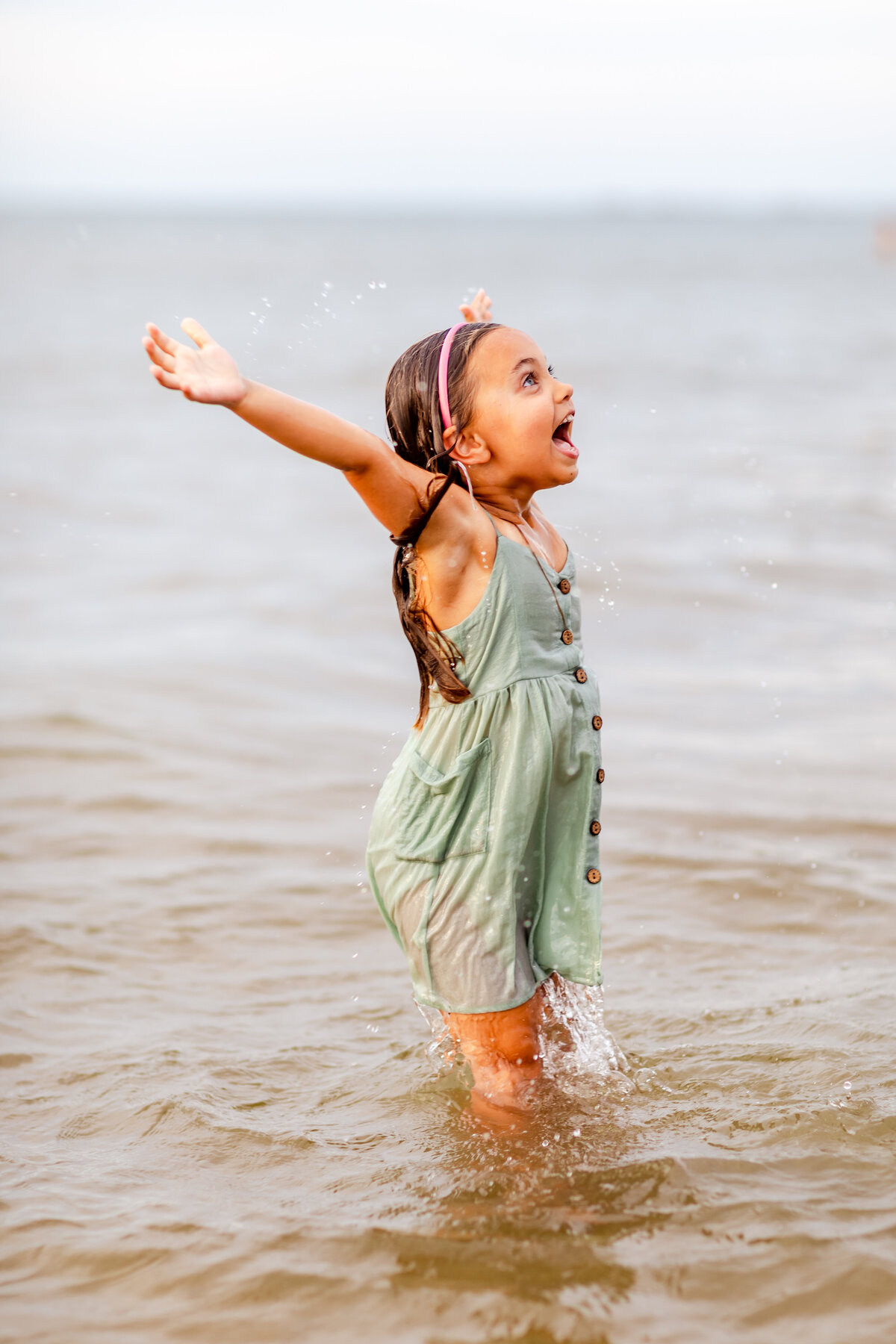 Candid, playful moment captured by Brooke Tucker as a little girl jumps out of the ocean, smiling brightly during a beach session in Hampton Roads, Virginia.