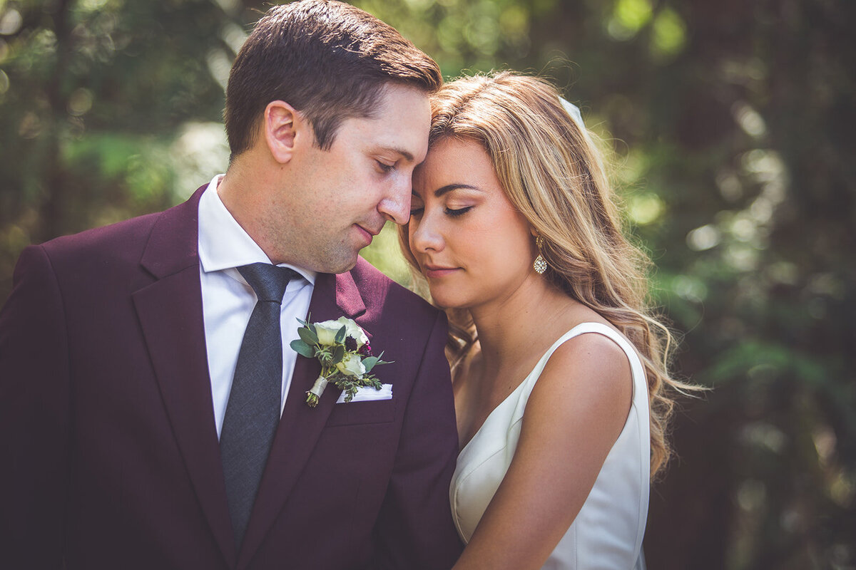 Wedding portrait of a bride with her eyes closed and a groom in a burgundy suit.