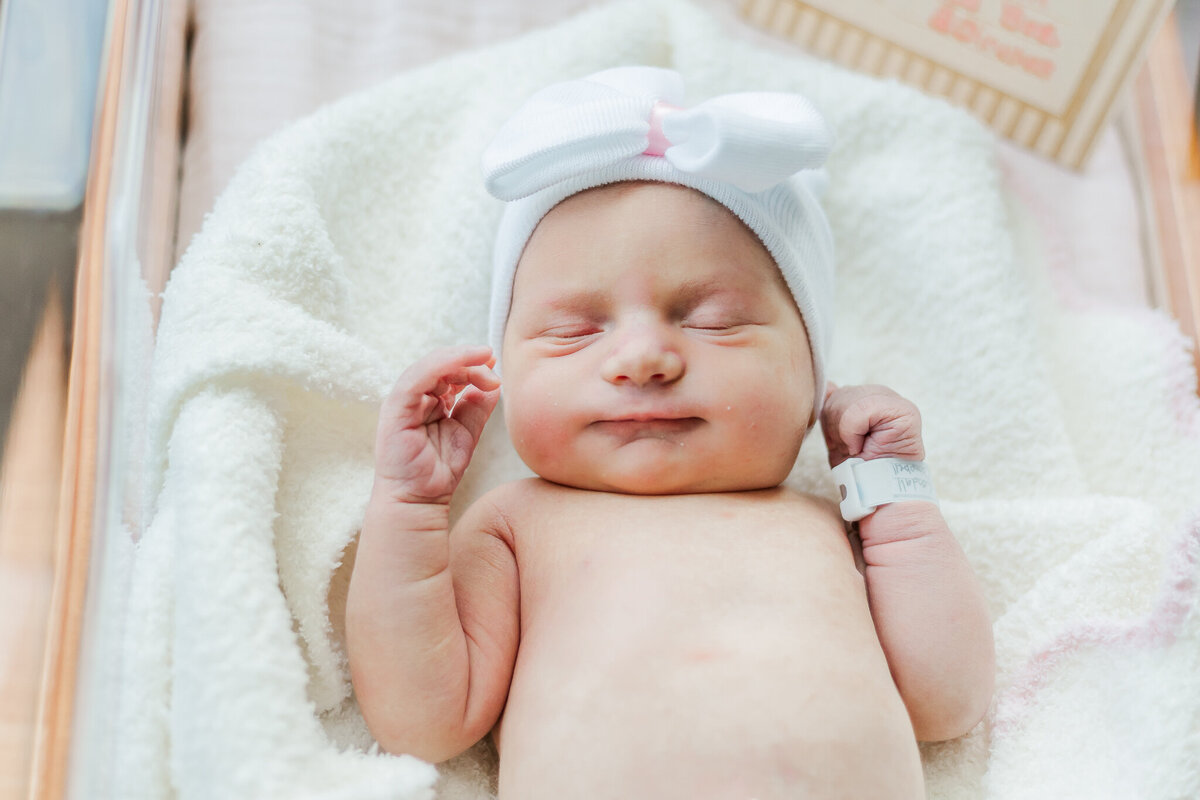Close up of newborn baby girl wearing white hat sleeping in hospital crib at Grandview medical center