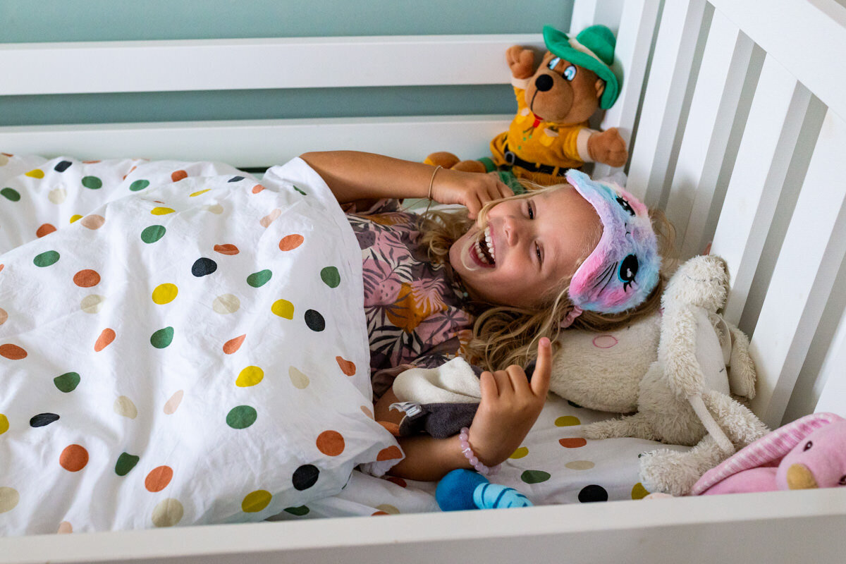 meisje ligt lachend in bed met slaapmasker
