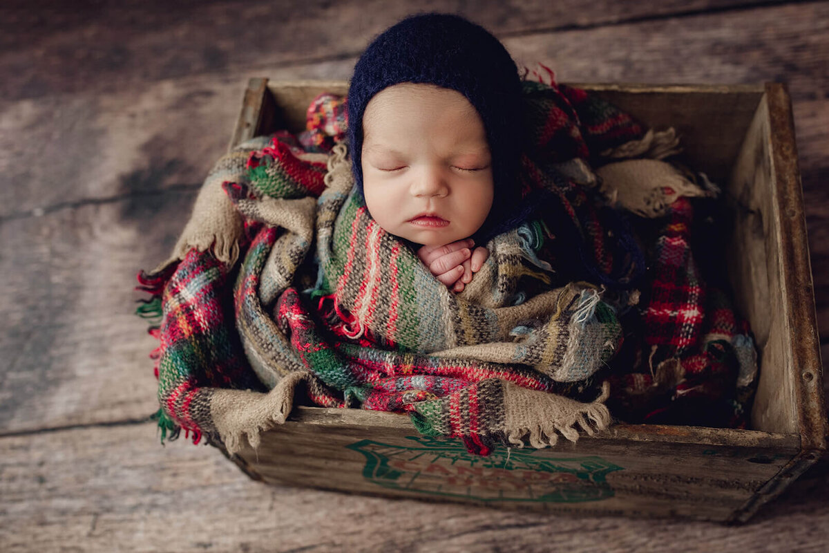 newborn boy wrapped in flannel inside a crate