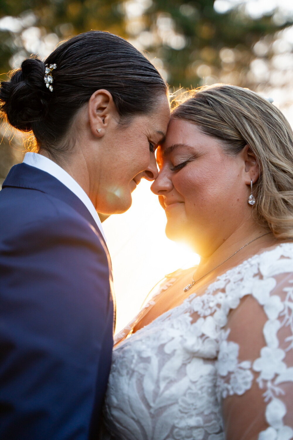 closeup image of a lesbian couple leaning foreheads against each other as sunlight shines through dramatically