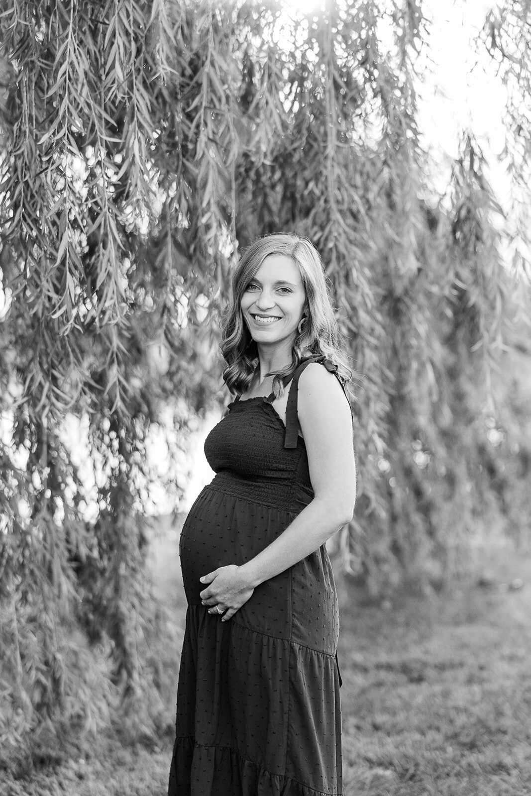 Pregnant woman smiling next to a willow tree