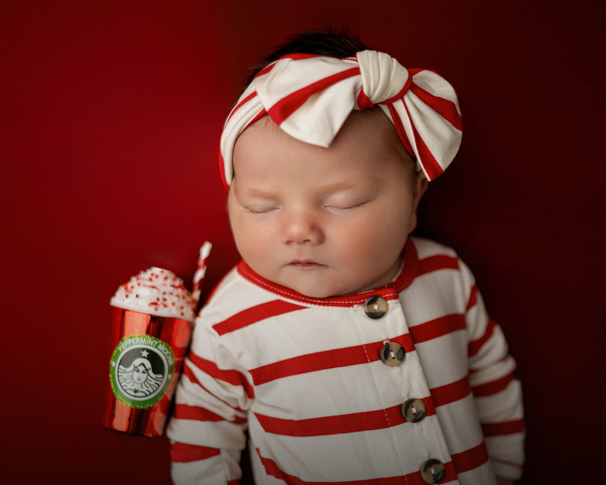 A newborn sleeps in red stripes onesie with christmas drink