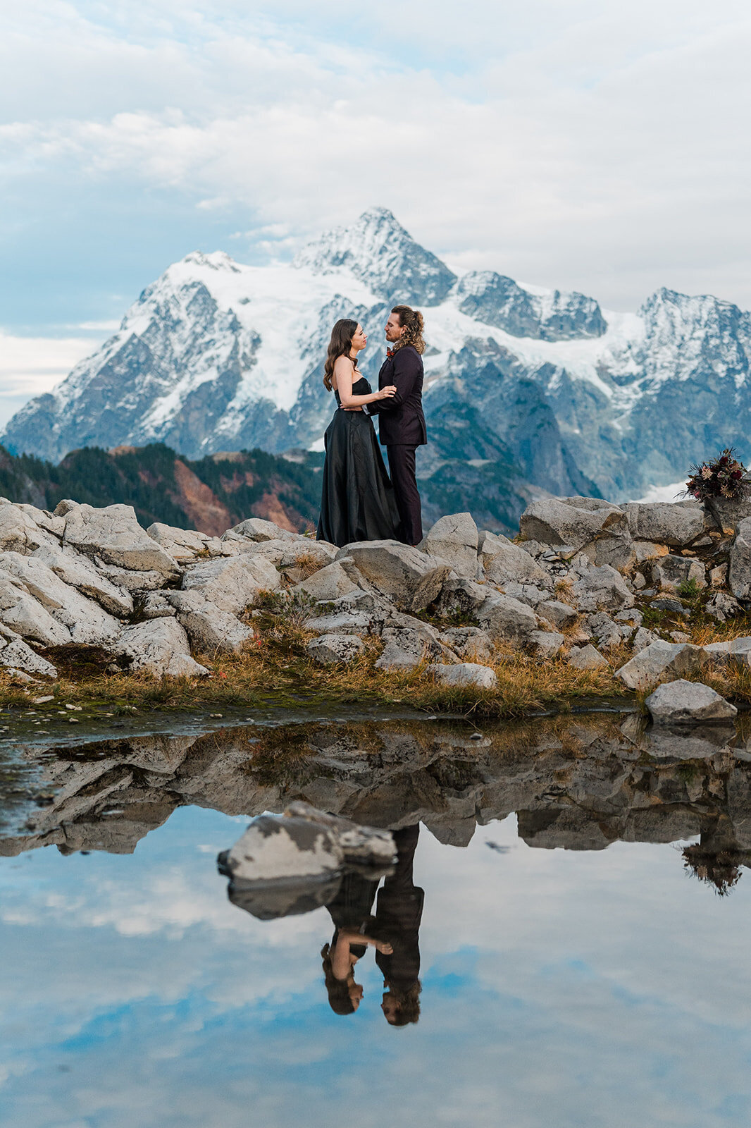 Bride in black dress & groom holding each other after elopement in front of Mount Shuksan in the North Cascades!
