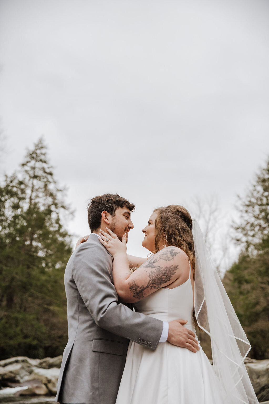 Bride and groom embracing and smiling at each other beneath overcast skies at Greenbrier, during their eloping to Gatlinburg wedding in the Smoky Mountains.
