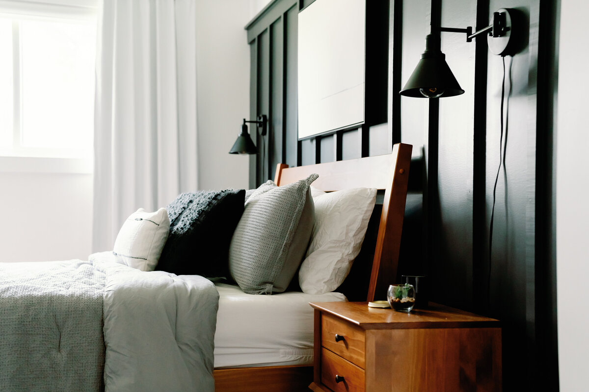 black wall mounted light fixtures on black board and batten feature wall in main bedroom with wood bed and side table