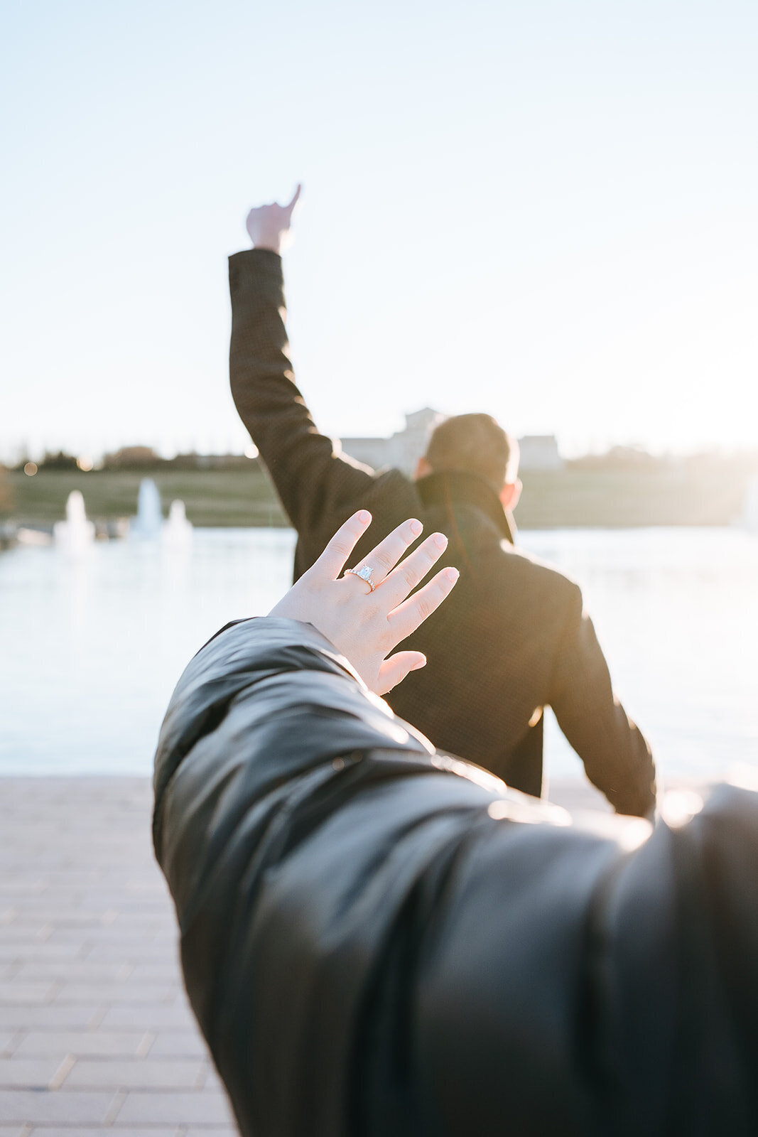 newly engaged woman showing off engagement ring while fiance celebrates