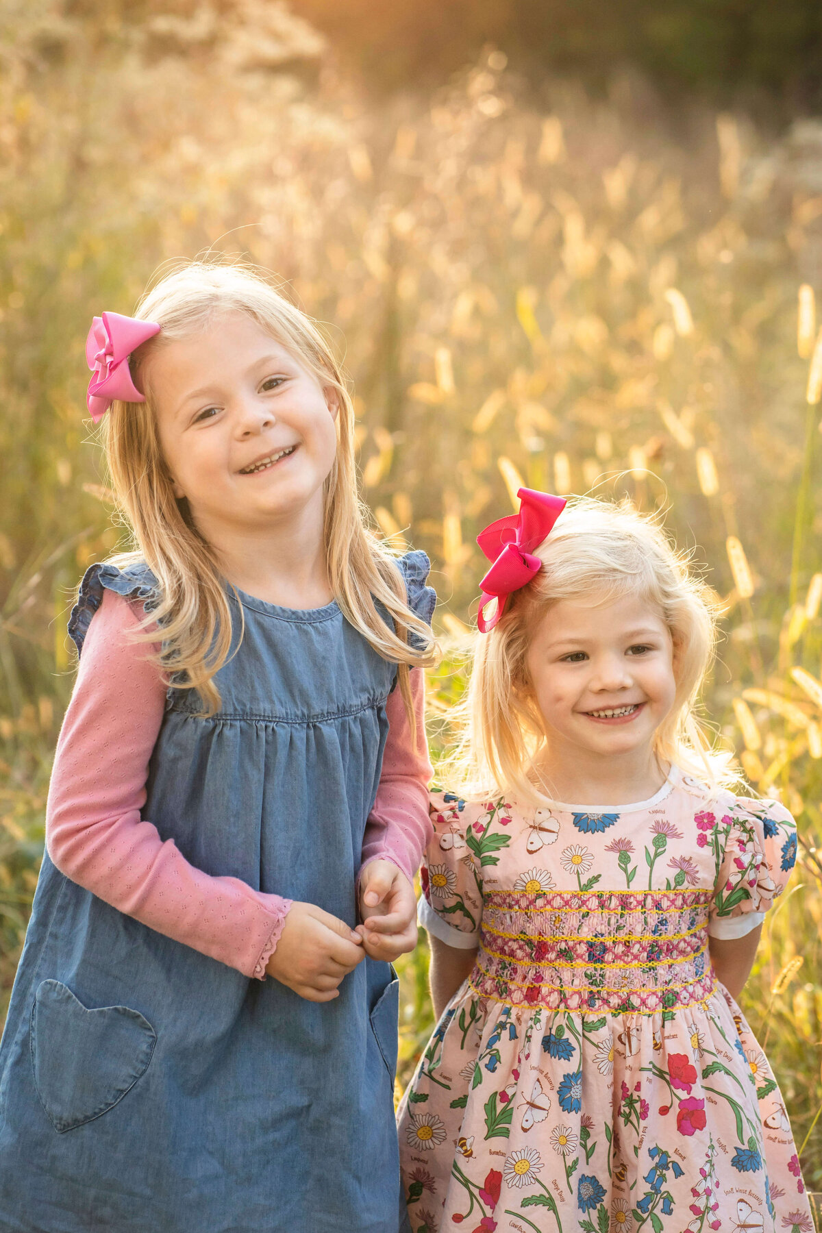 2 young sisters smiling at the camera during sunset in a field of tall grass