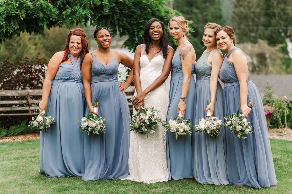 Bride-and-bridesmaids-laugh-for-photos-on-wedding-day-at-venue-Green-Gates-at-Flowing-Lake-in-Snohomish-WA-photo-by-Joanna-Monger-Photography