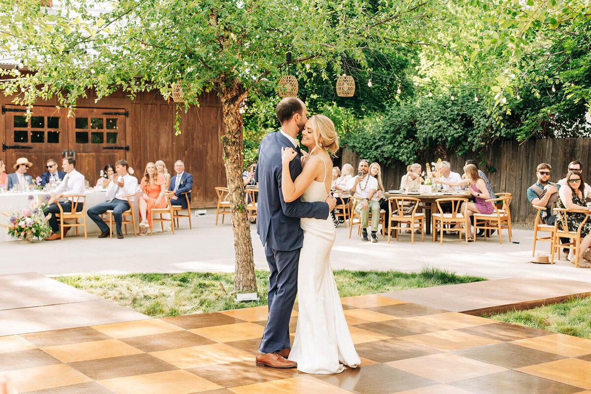 A bride and groom dancing on a dance floor at a backyard wedding reception.