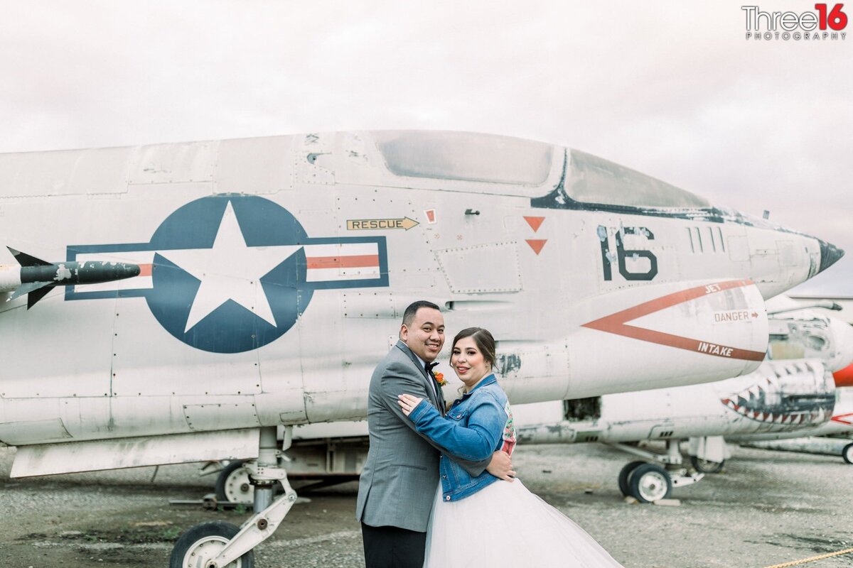 Newly married couple embrace one another as they smile for the camera in front of a vintage plane