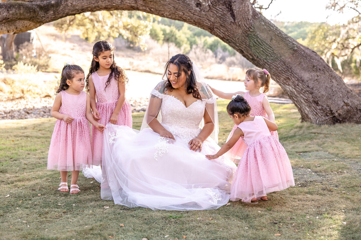 bride kneels with 4 toddler flower girls in pink dresses at Hayes Hollow at Hidden Falls wedding in Spring Branch Texas