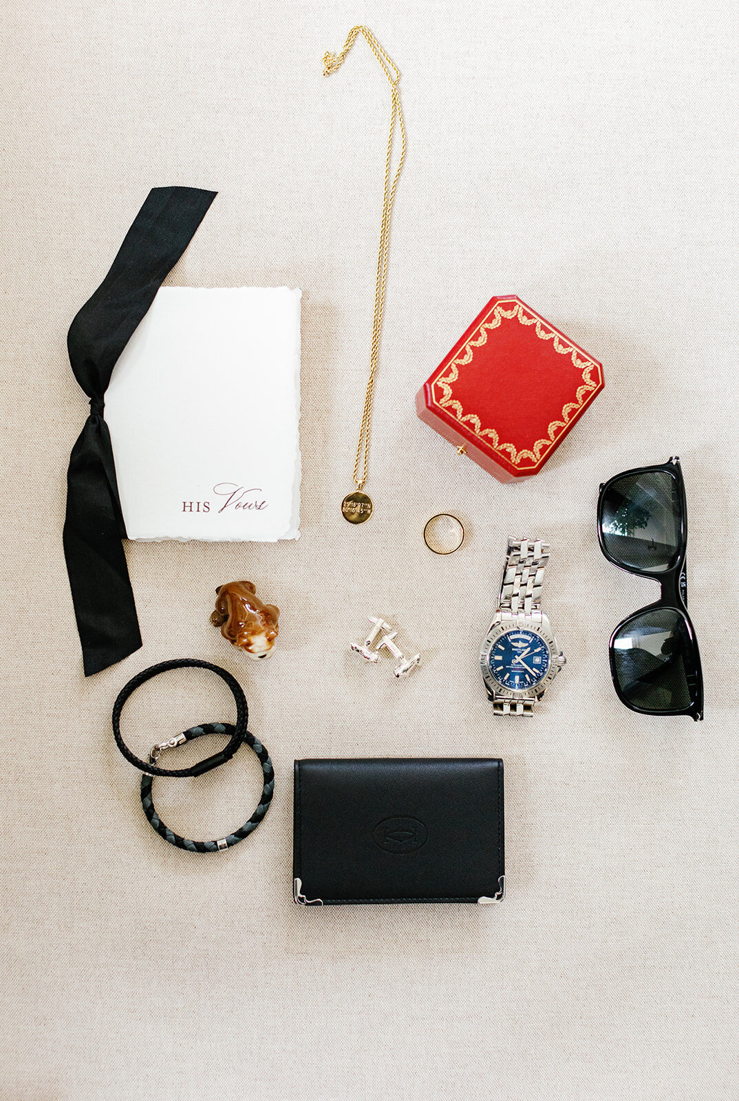 A flat lay of the groom's black vows book, watch, cufflinks, sunglasses, and other accessories styled for Ashley and Cameron's micro wedding at Ocean Reef in Key Largo, captured by Claudia Amalia Photography.