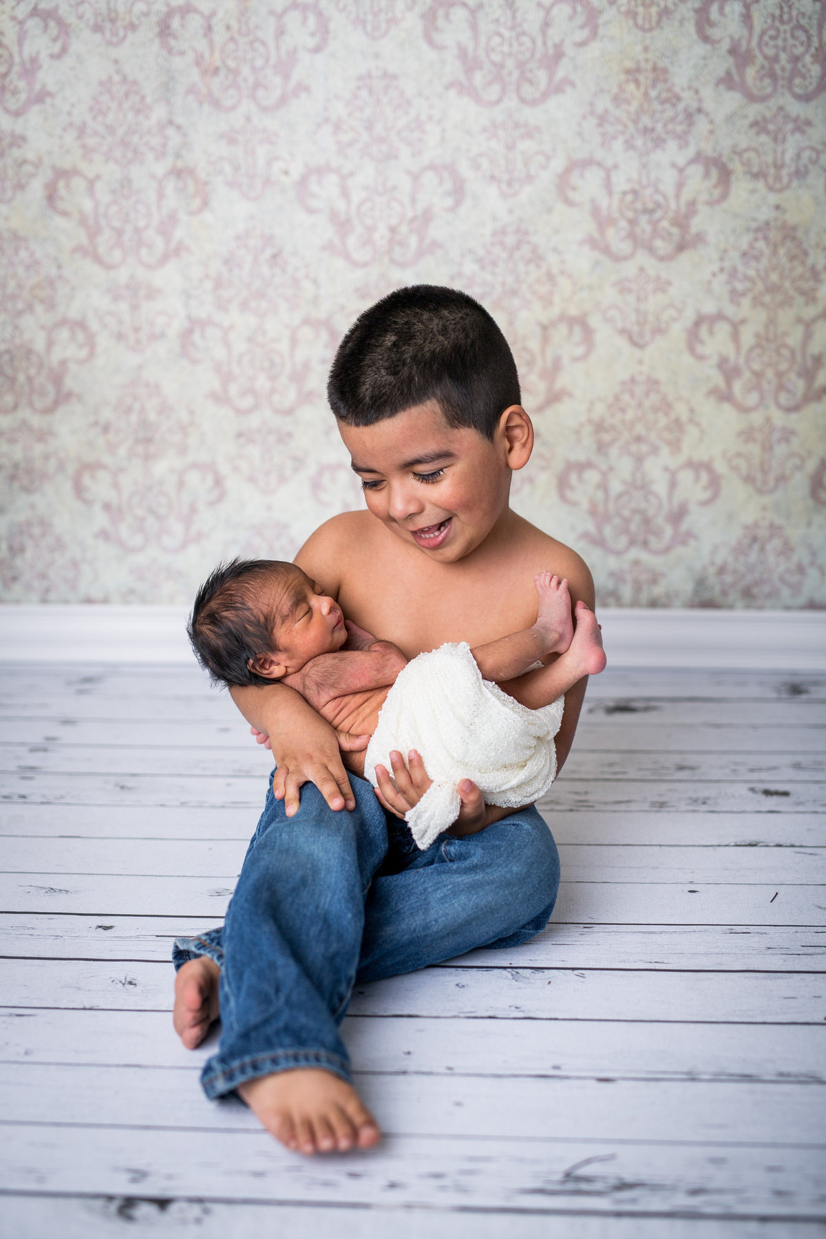 Brother holding newborn sister in his arms on s wooden floor in a photography studio