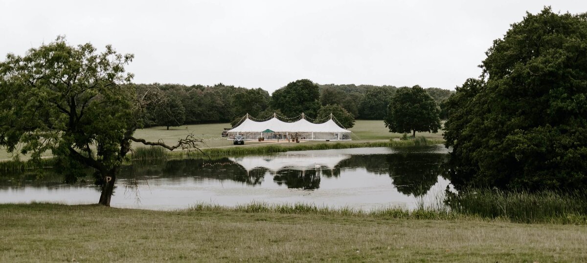 A large pole marquee in a field behind a lake with stunning country views