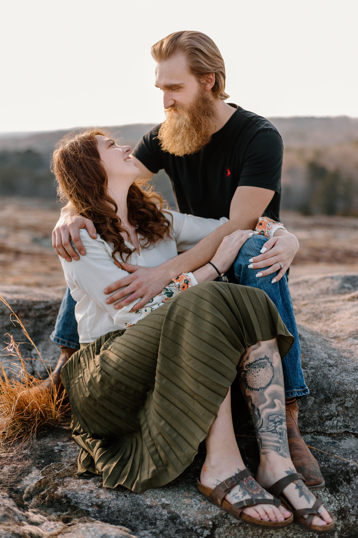 engaged couple sitting on a rock laughing