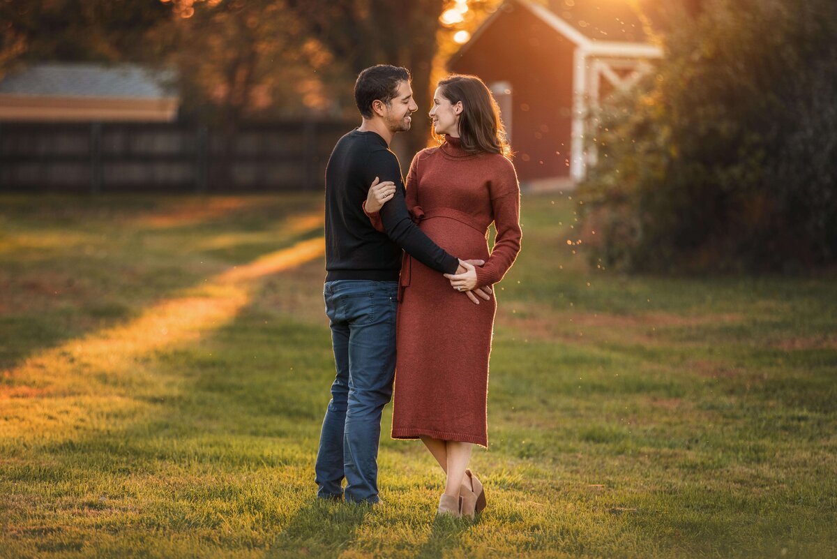 Expecting couple looking at each other with barn behind them